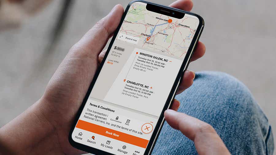 An owner-operator holding a cell phone that displays a load to book on the Schneider FreightPower app